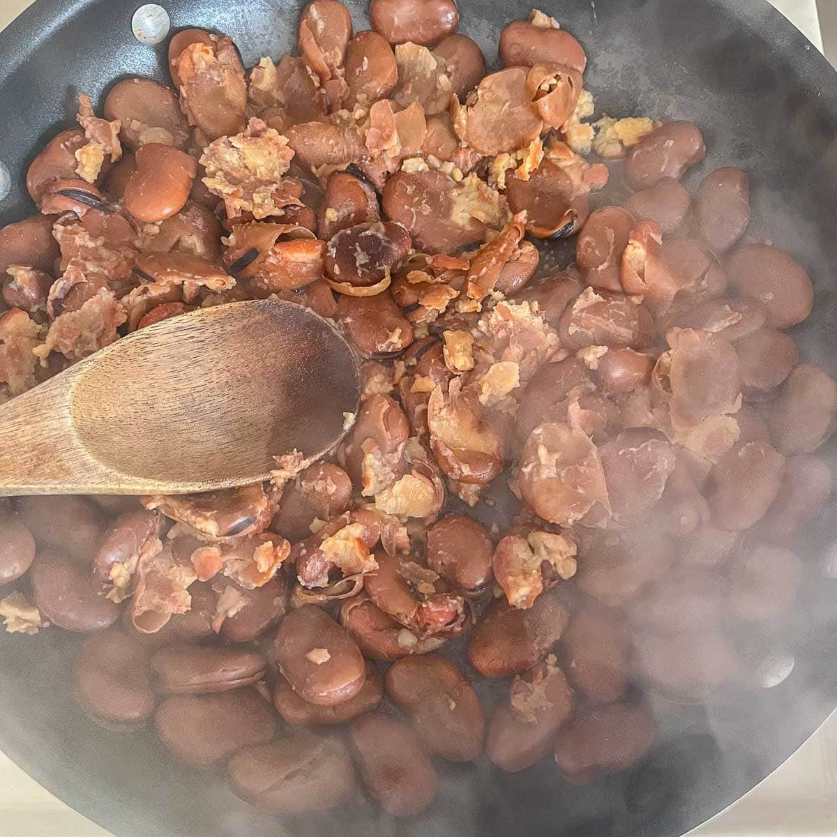 mashing fava beans in a pan