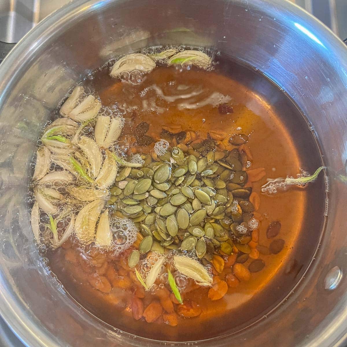 a pot of oil with garlic and seeds