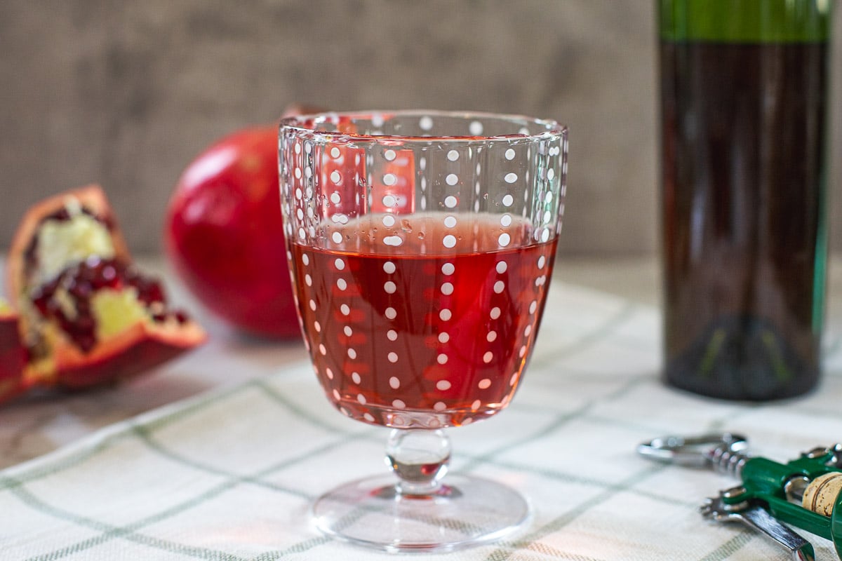 a glass of wine with pomegranates next to it