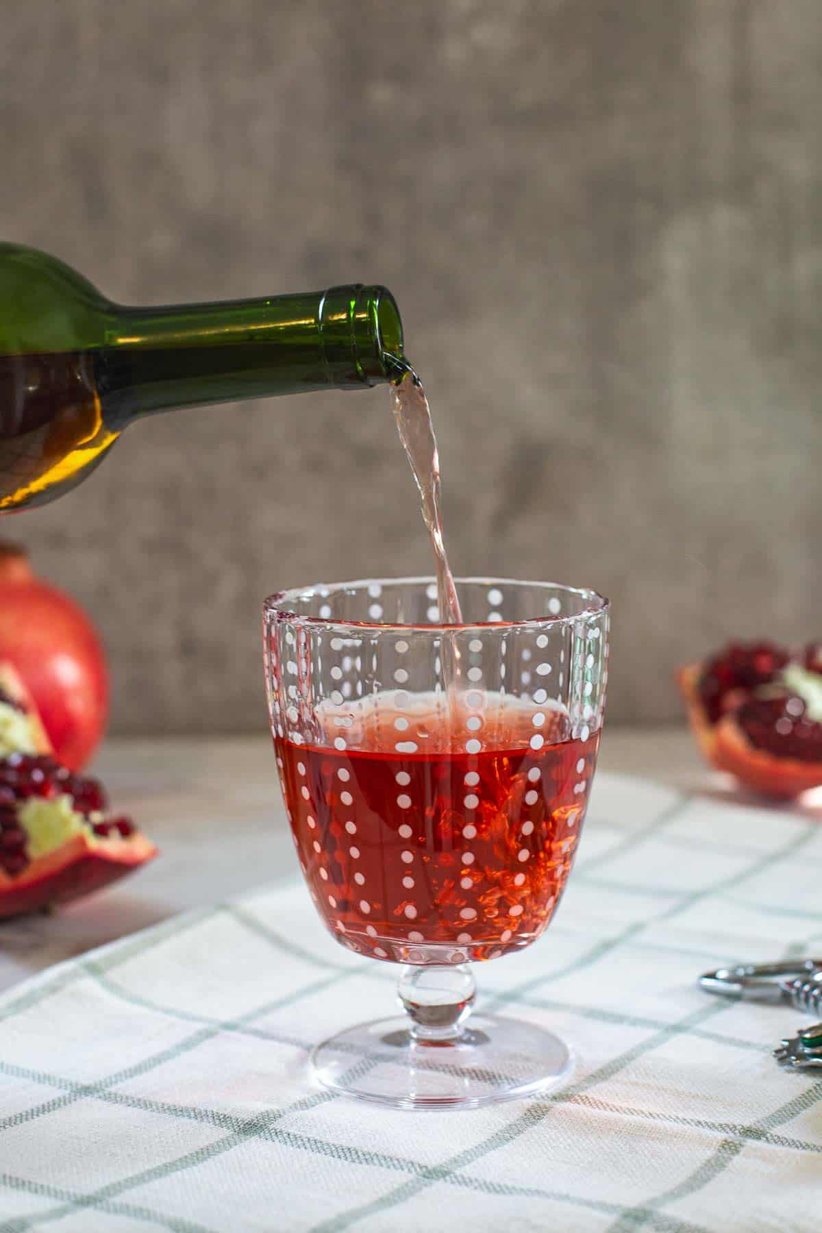 wine bottle pouring pomegranate wine into goblet with split pomegranates on the side