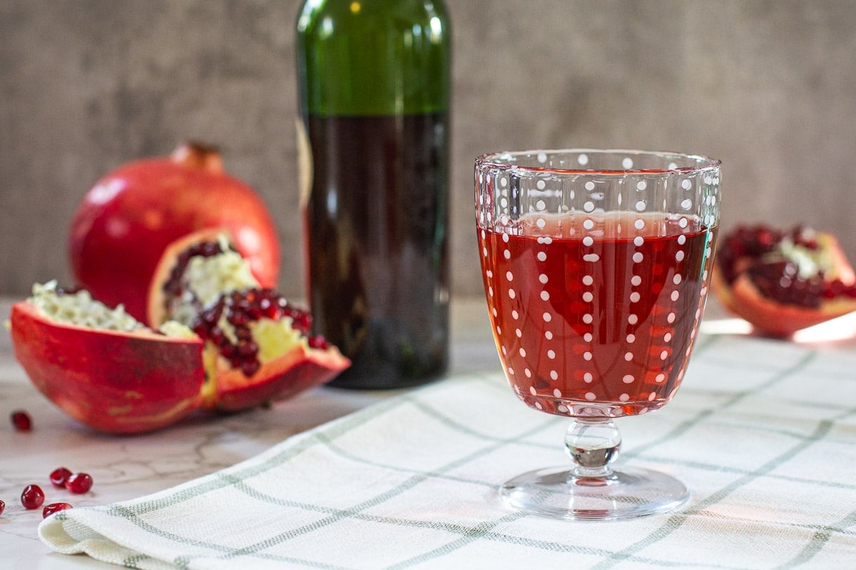 pomegranate wine in goblet beside split pomegranate and wine bottle