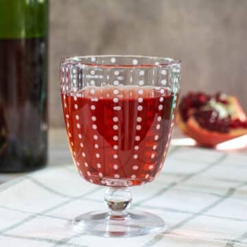 pomegranate wine in goblet beside split pomegranate and wine bottle
