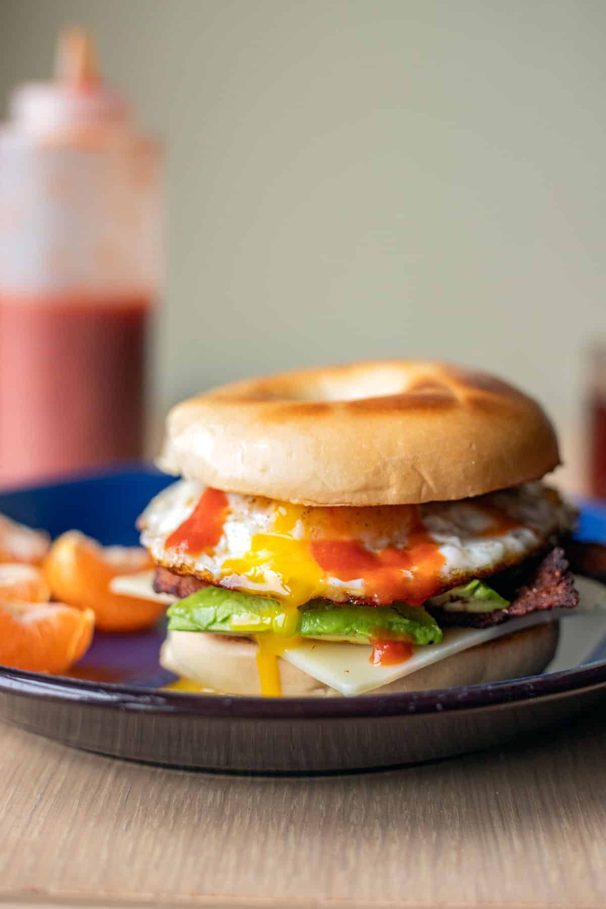 a breakfast bagel sandwich on a blue plate with orange slices