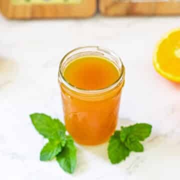 orange syrup in mason jar surrounded by lemons, oranges, mint