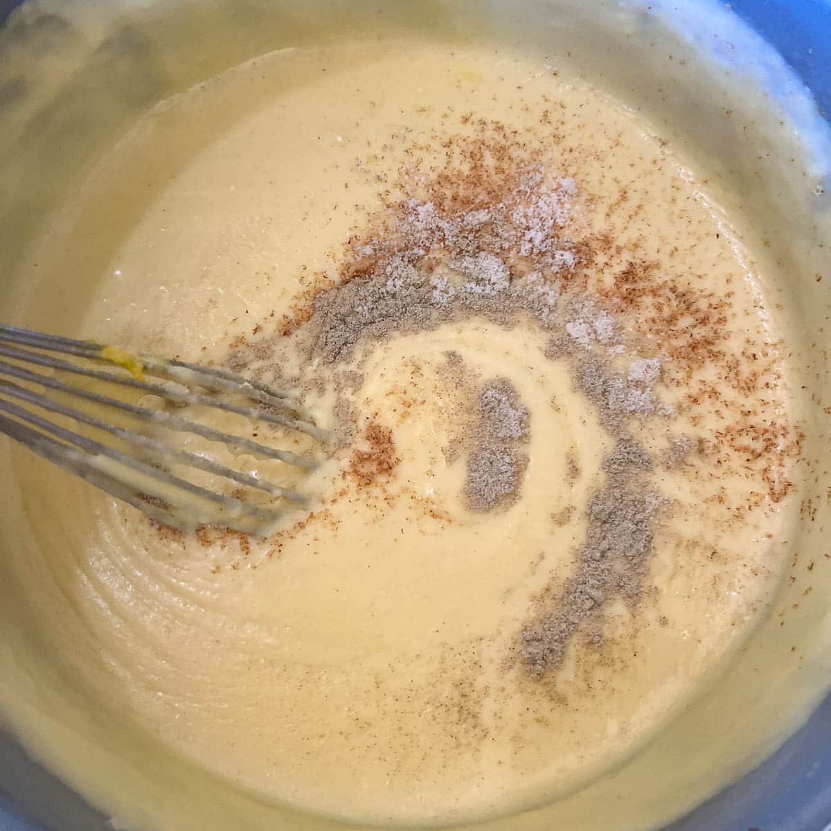 adding spices to béchamel sauce in a pot.