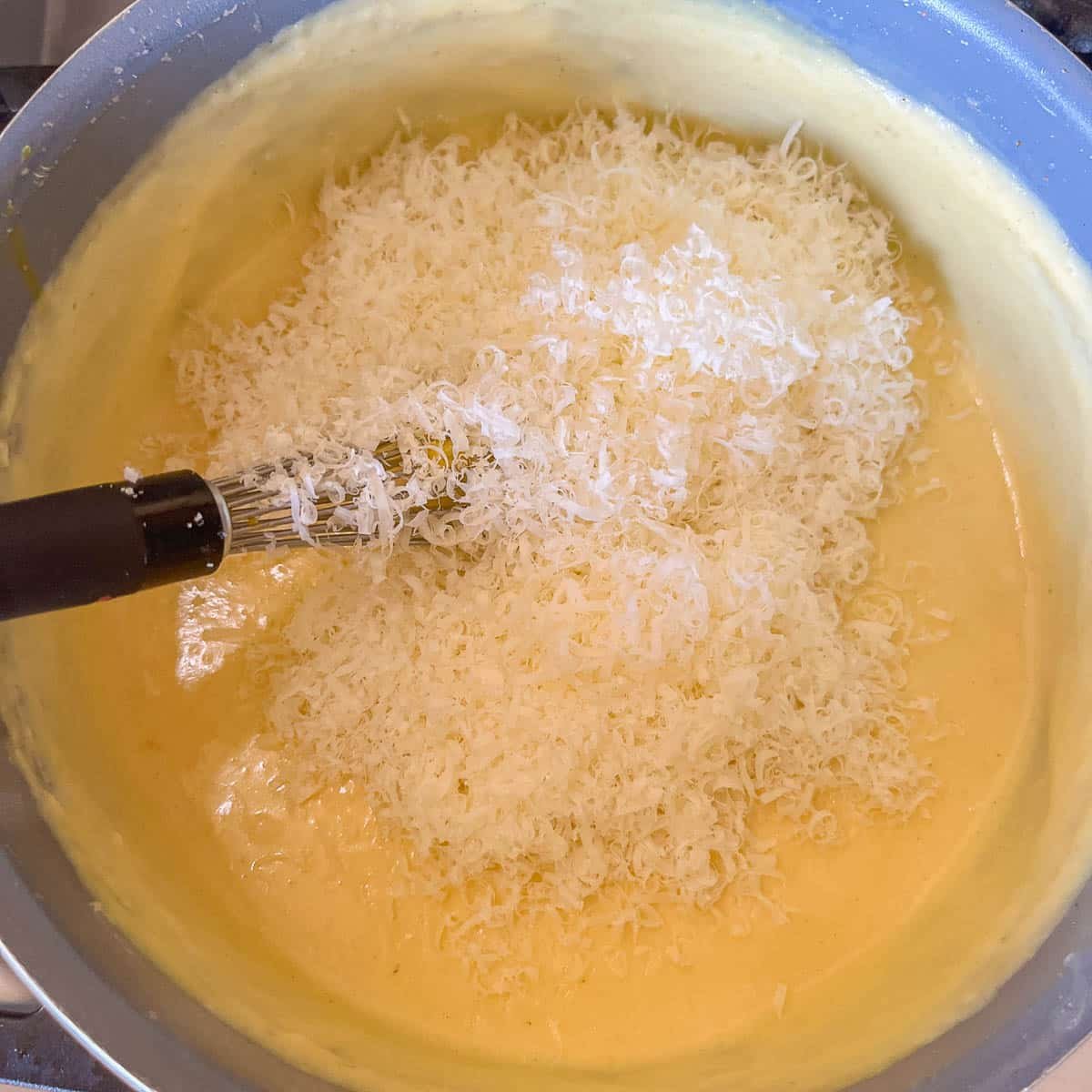 adding cheese to béchamel sauce in a pot.