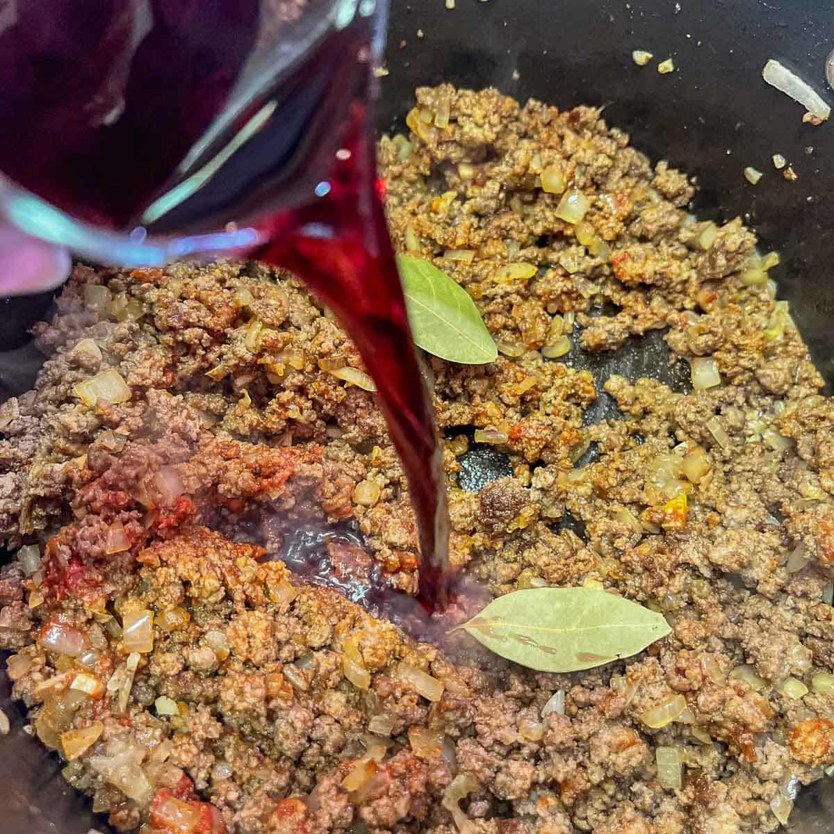 pouring wine in a pot with ground meat.