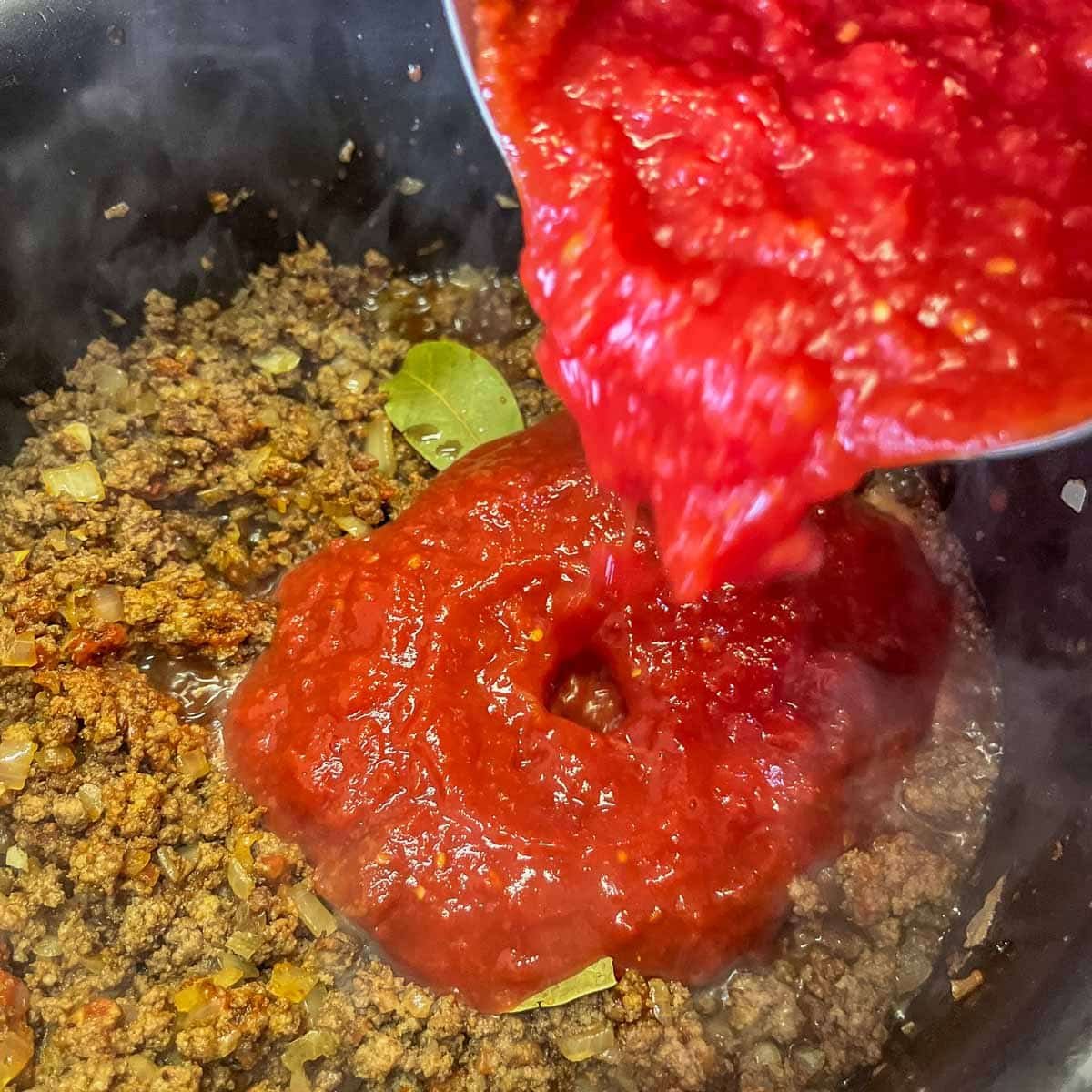 pouring crushed tomatoes to a pot of sauce.