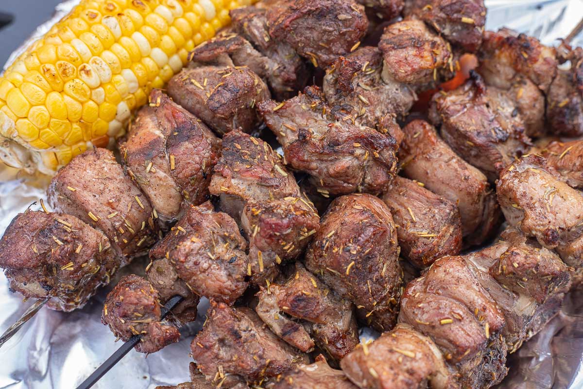 lamb shish kabobs beside corn on the cob