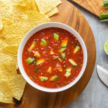 ranchera salsa in bowl next to chips, limes, knife, herbs