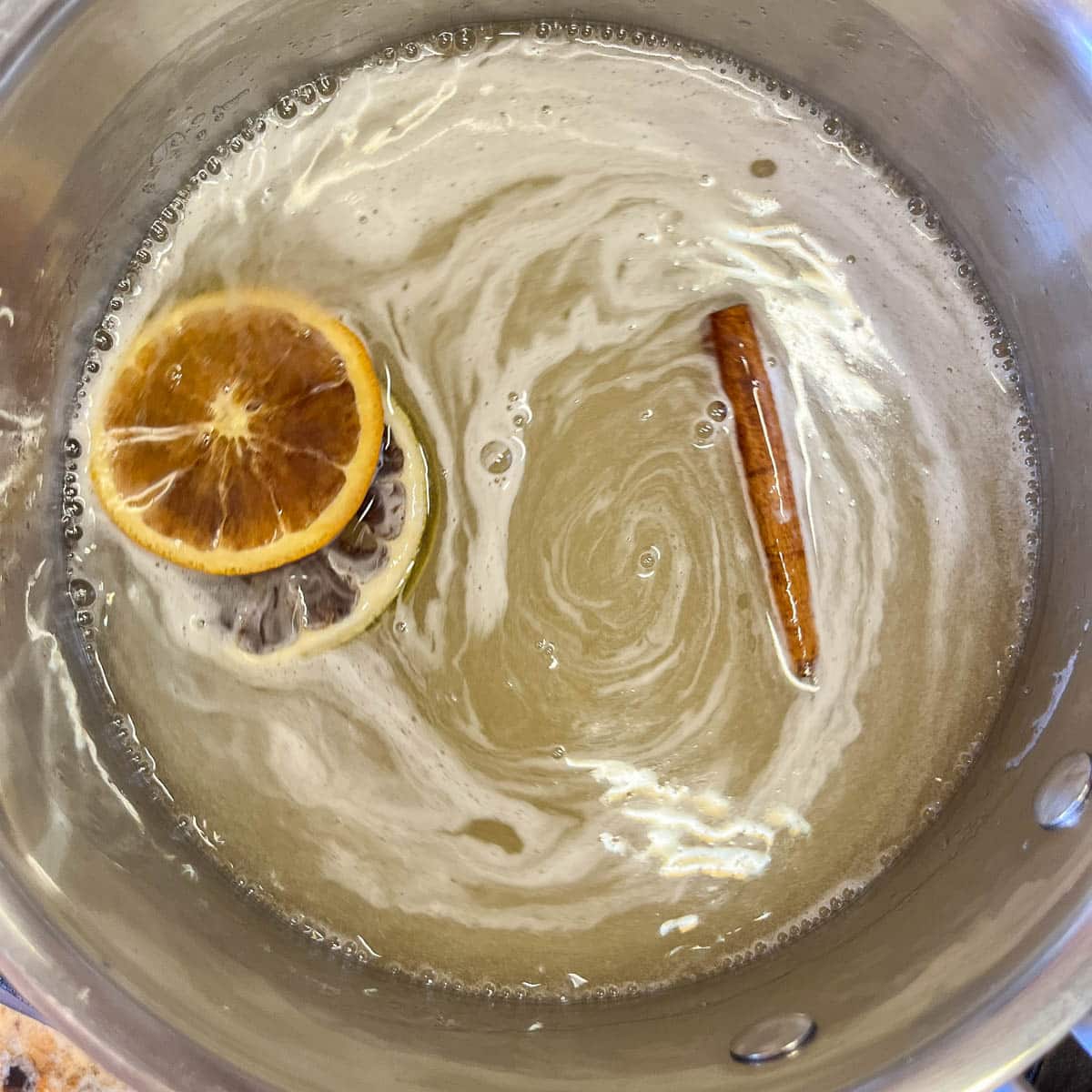 syrup simmering in a saucepan with cinnamon stick and orange slices.