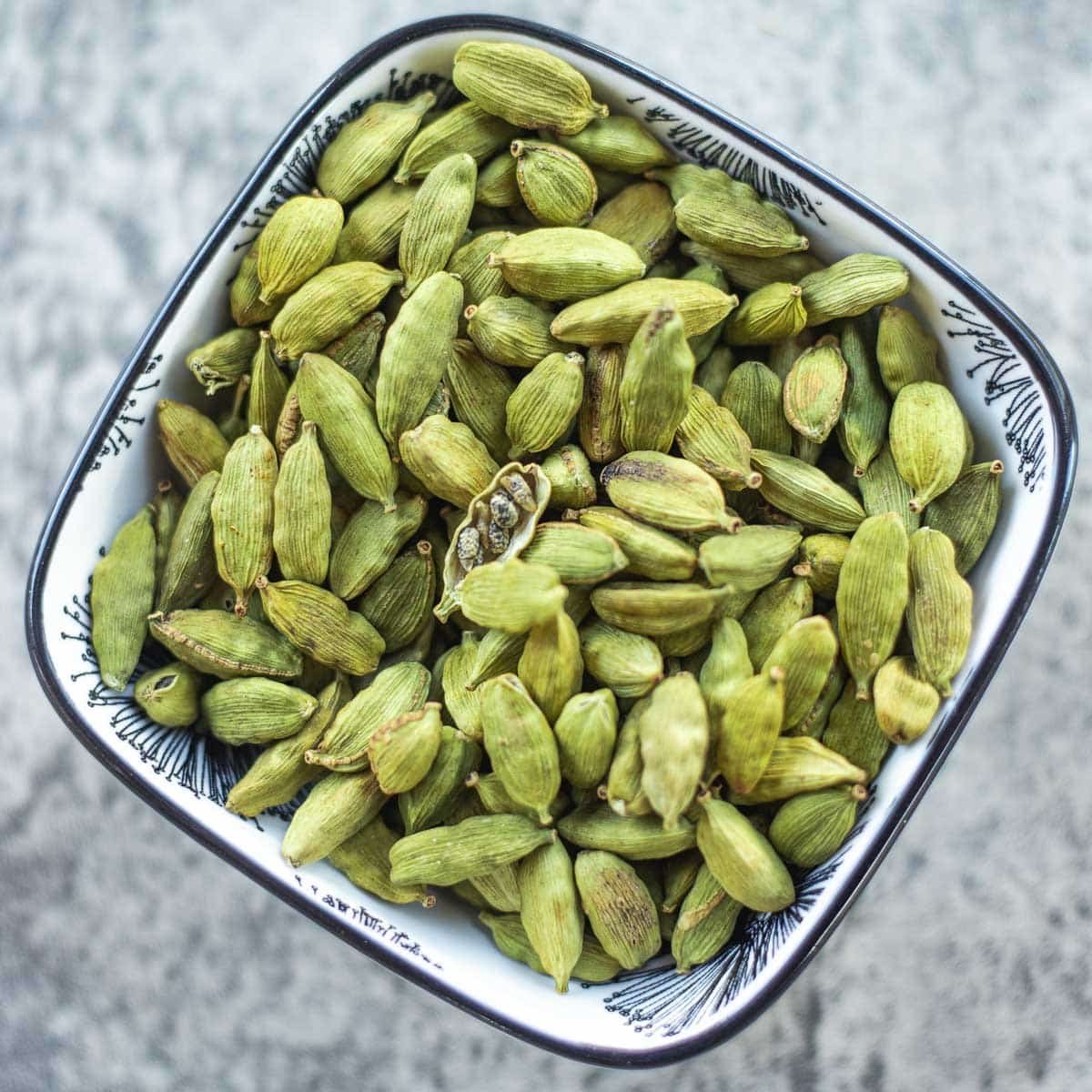 green cardamom pods in bowl with one split open revealing seeds