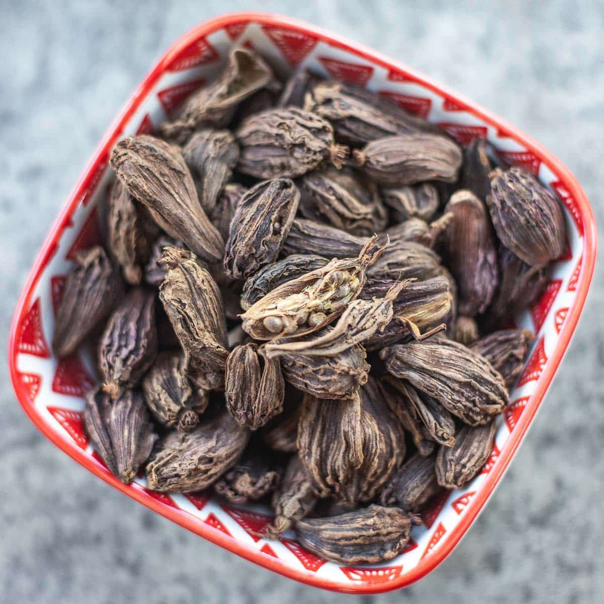 black cardamom pods in bowl with one split open revealing seeds