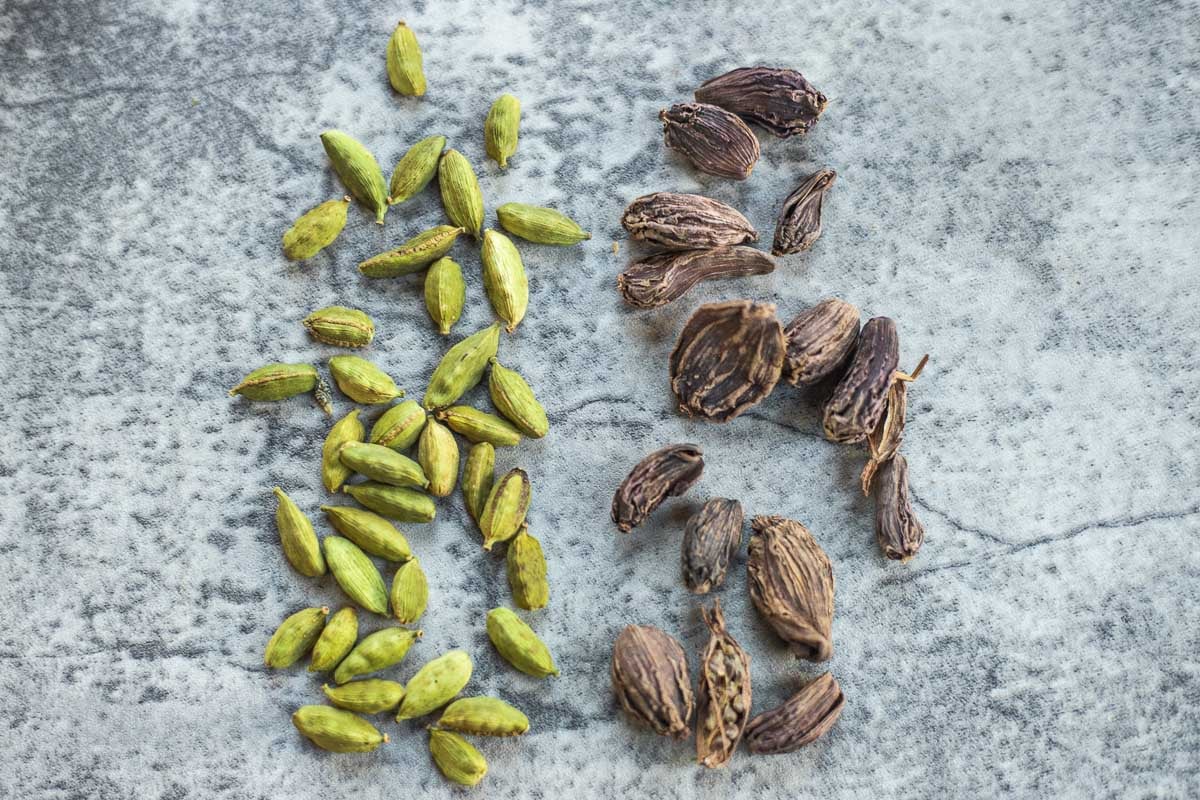 dozens of green and black cardamom pods laid out on the counter side by side