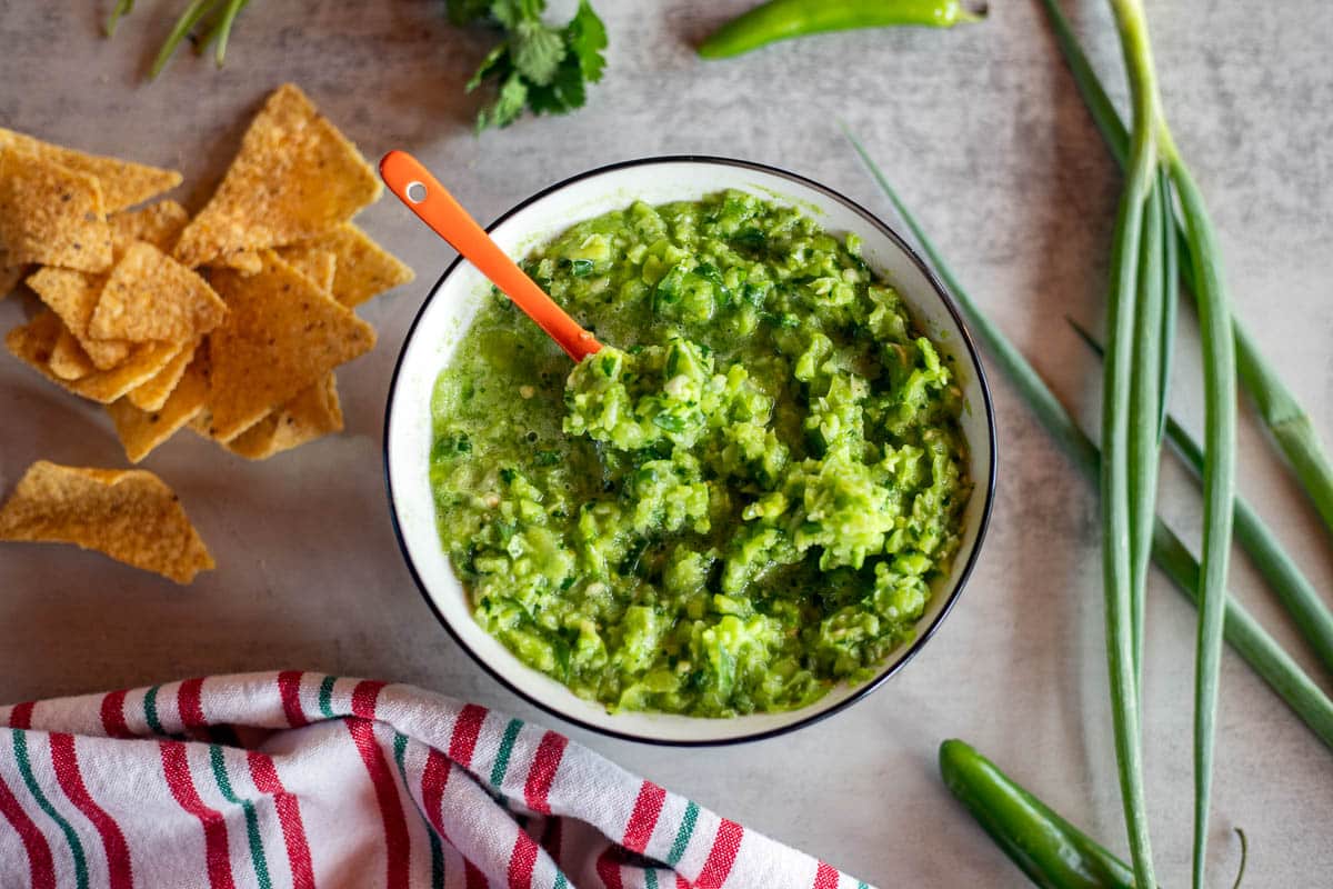 green tomato salsa with chips and veggies scattered around it