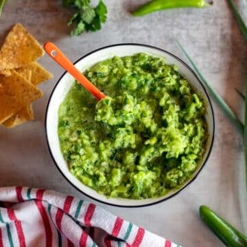 green tomato salsa in a bowl with chips and ingredients around it