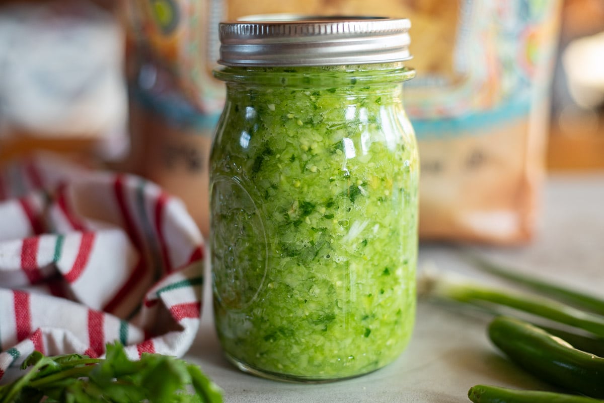 green salsa ingredients in a jar with chips and other ingredients around it.