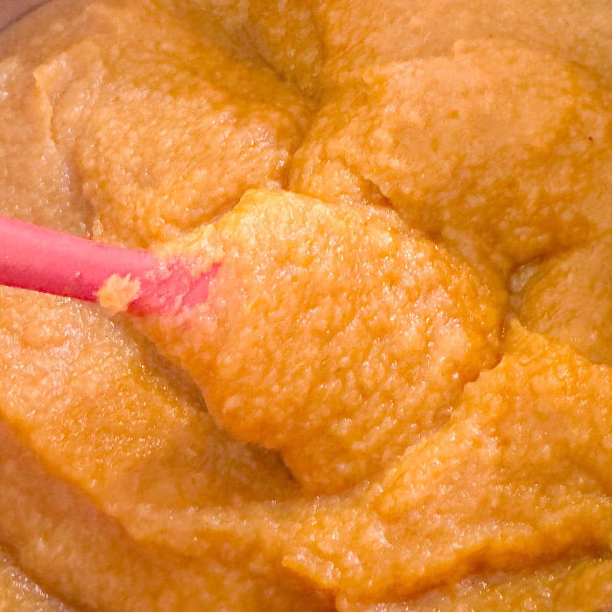 crabapple sauce being stirred with red spatula 