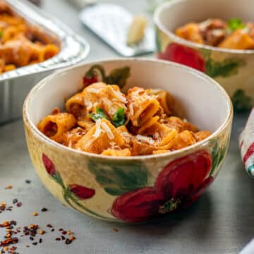 rigatoni in bowls with more in a pan behind it