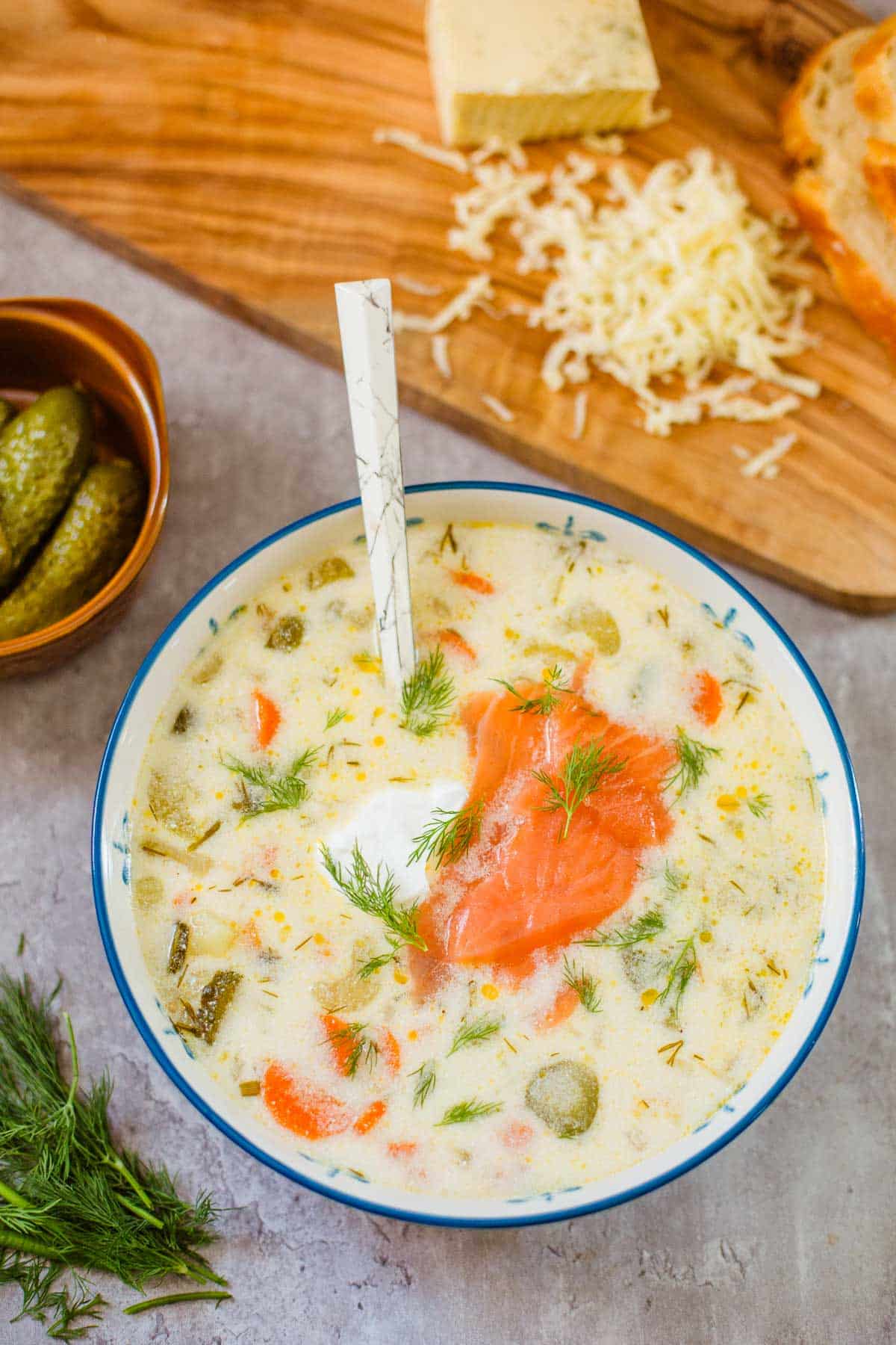 zupa ogorkowa (polish dill pickle soup) in bowl beside pickles, dill, shredded cheese