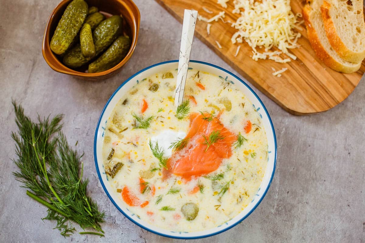 zupa ogorkowa (polish dill pickle soup) in bowl beside pickles, dill, shredded cheese