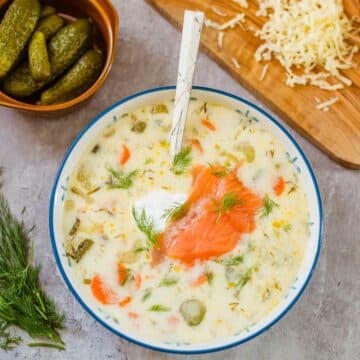 zupa ogorkowa in bowl beside pickles, dill, shredded cheese