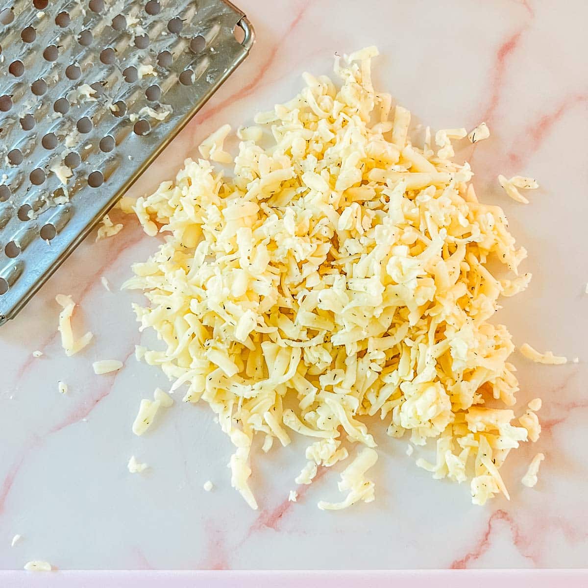 shredded dill havarti on cutting board beside cheese grater