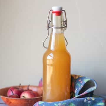 apple cider vinegar in a fliptop bottle with a blue dish cloth and apples in a bowl