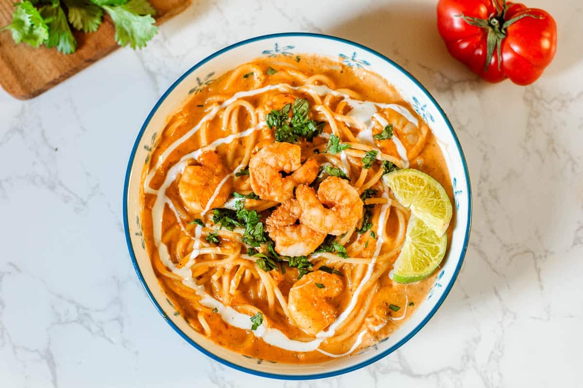 creamy shrimp pasta in bowl with lime slices beside veggies