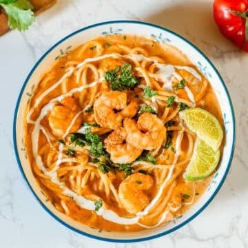 creamy shrimp pasta in bowl with lime slices beside veggies