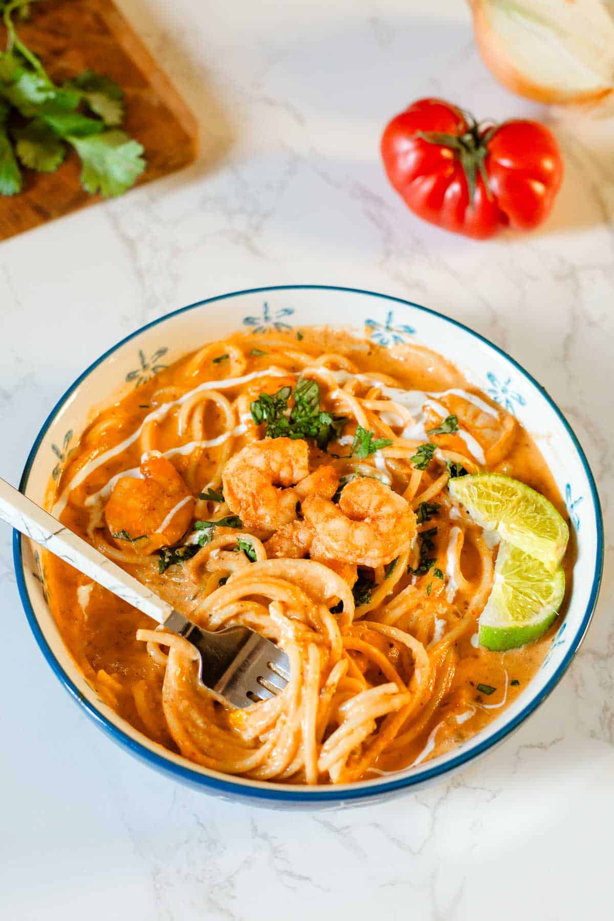 creamy shrimp pasta in bowl with fork and lime slices beside veggies