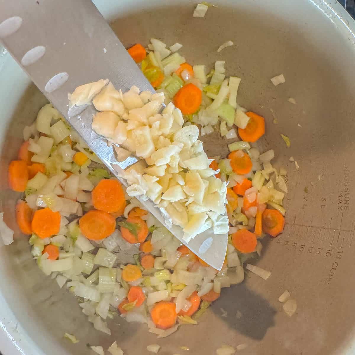 garlic being added to a pot of chopped carrots, celery, and onions