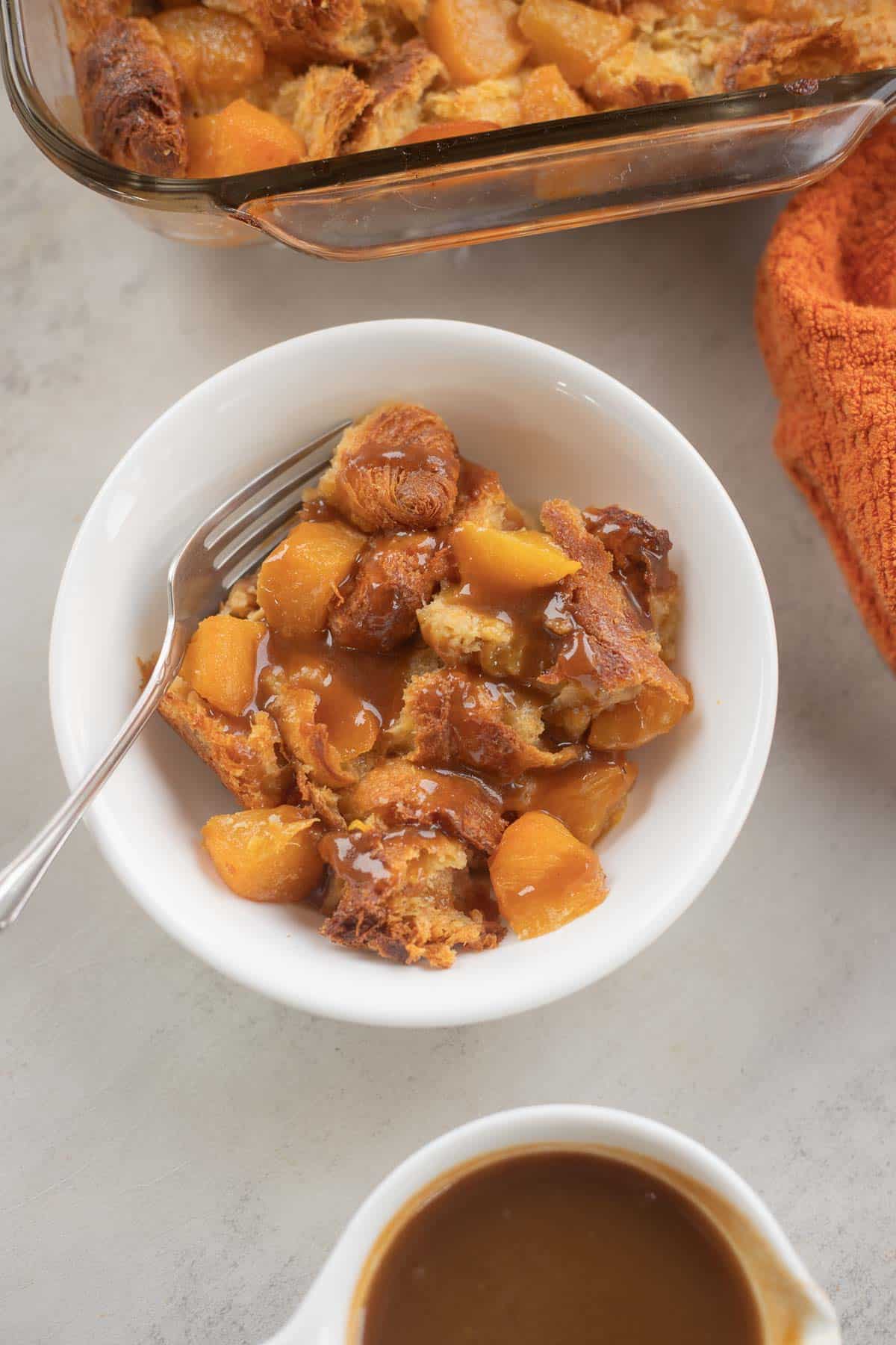 peach bread pudding with caramel sauce in a white bowl