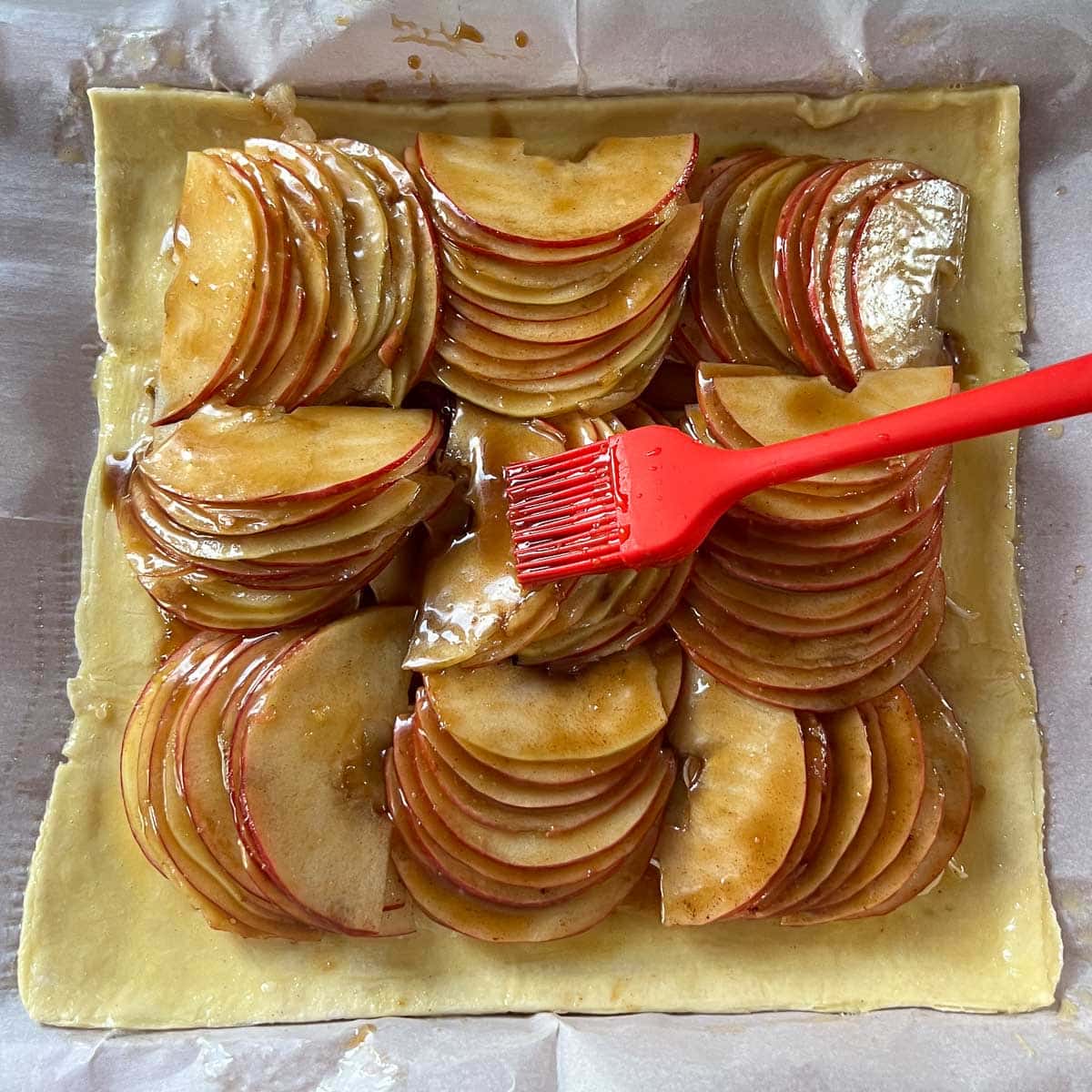 brushing caramel sauce on apples atop puff pastry tart