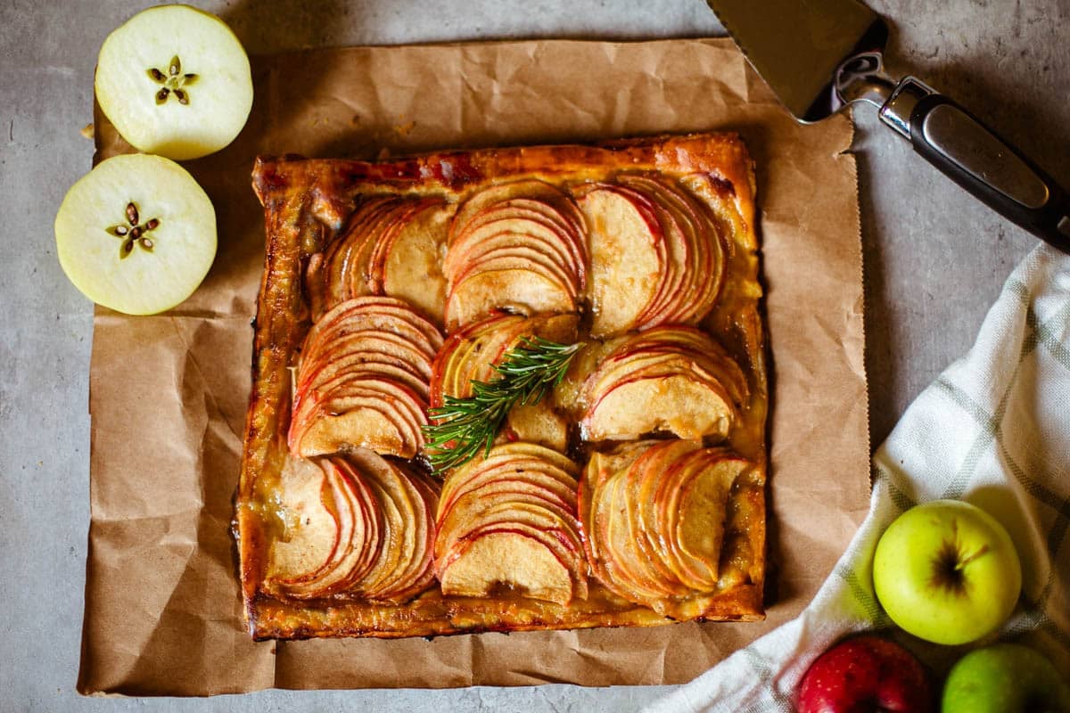 apple tart using puff pastry on brown paper beside apples