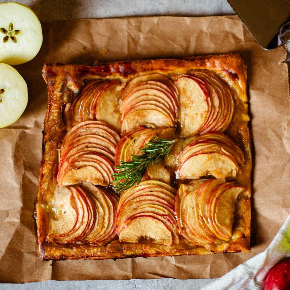 apple puff pastry tart on brown paper beside apples.