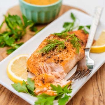 partially flaked salmon fillet with fresh herbs, lemon slices, and fork.