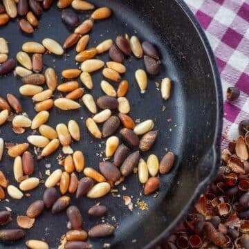 roasted pine nuts in a pan with shells next to it.