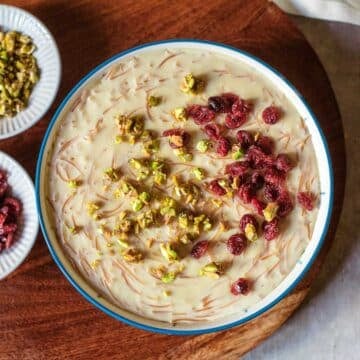 seviyan in bowl with chopped pistachios and craisins on top and in small dishes off to the side.