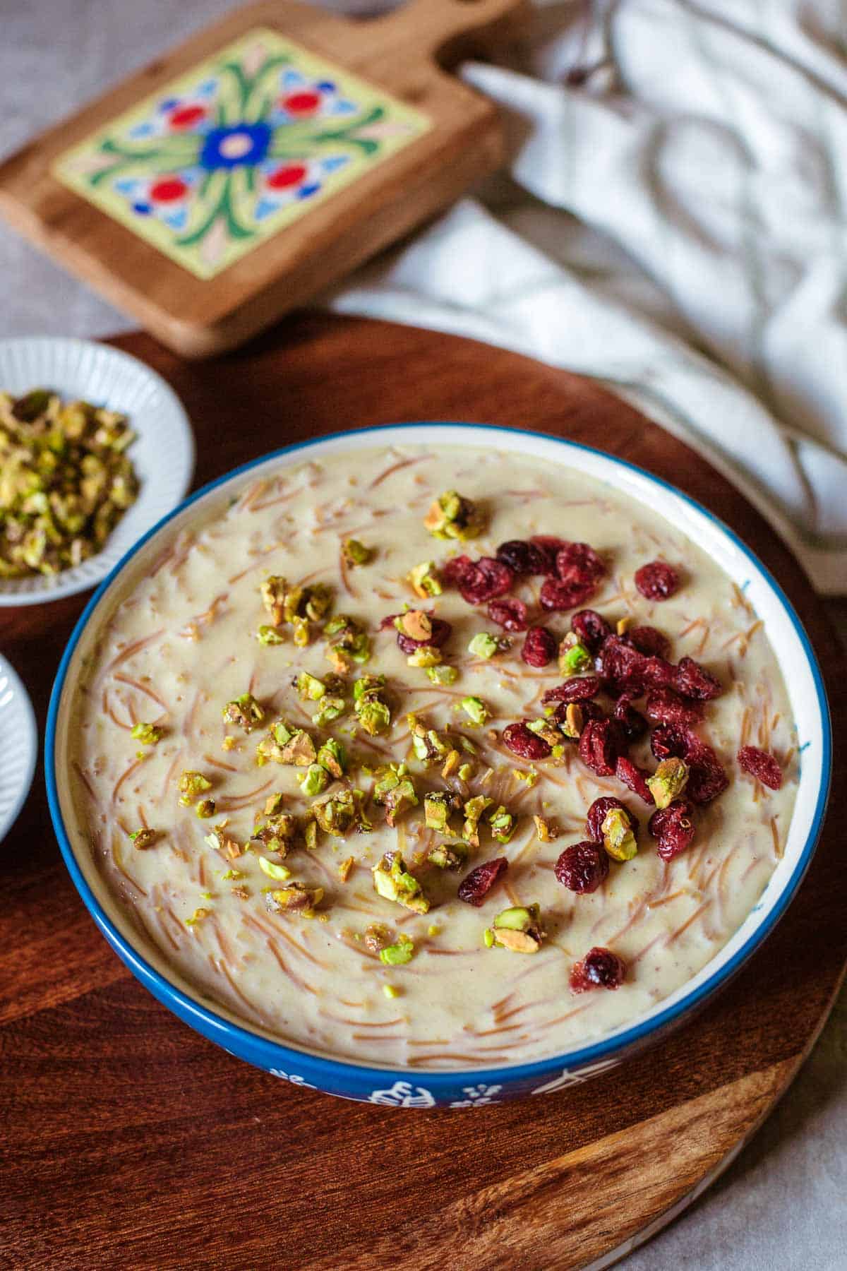 shemai in bowl topped with craisins and pistachios beside colored tile.