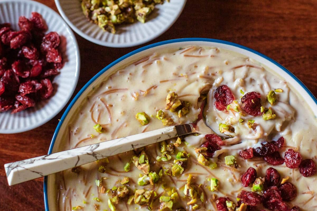 spoon and bowl full of seviyan (sweet vermicelli dessert) topped with chopped pistachios and craisins.