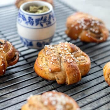 kardemummabullar on a cooling rack with a just of cardamom pods.