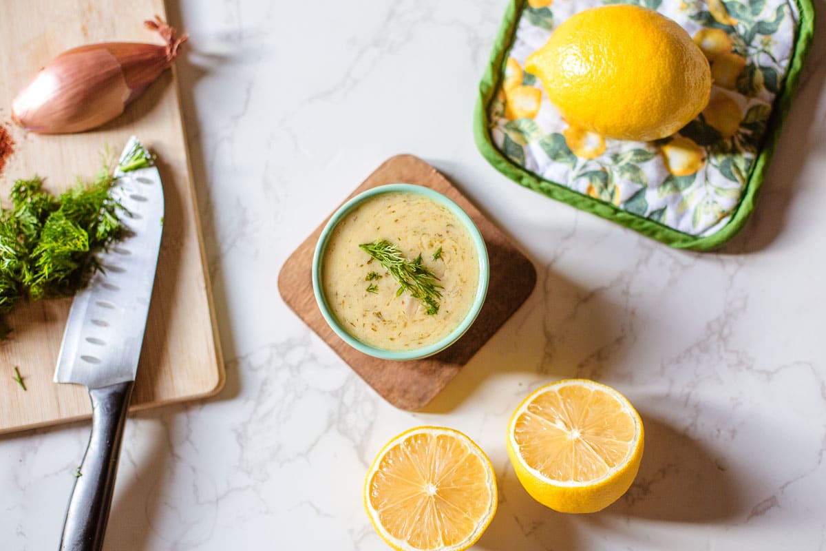 lemon dill sauce beside lemons, shallot, chopped dill, knife.