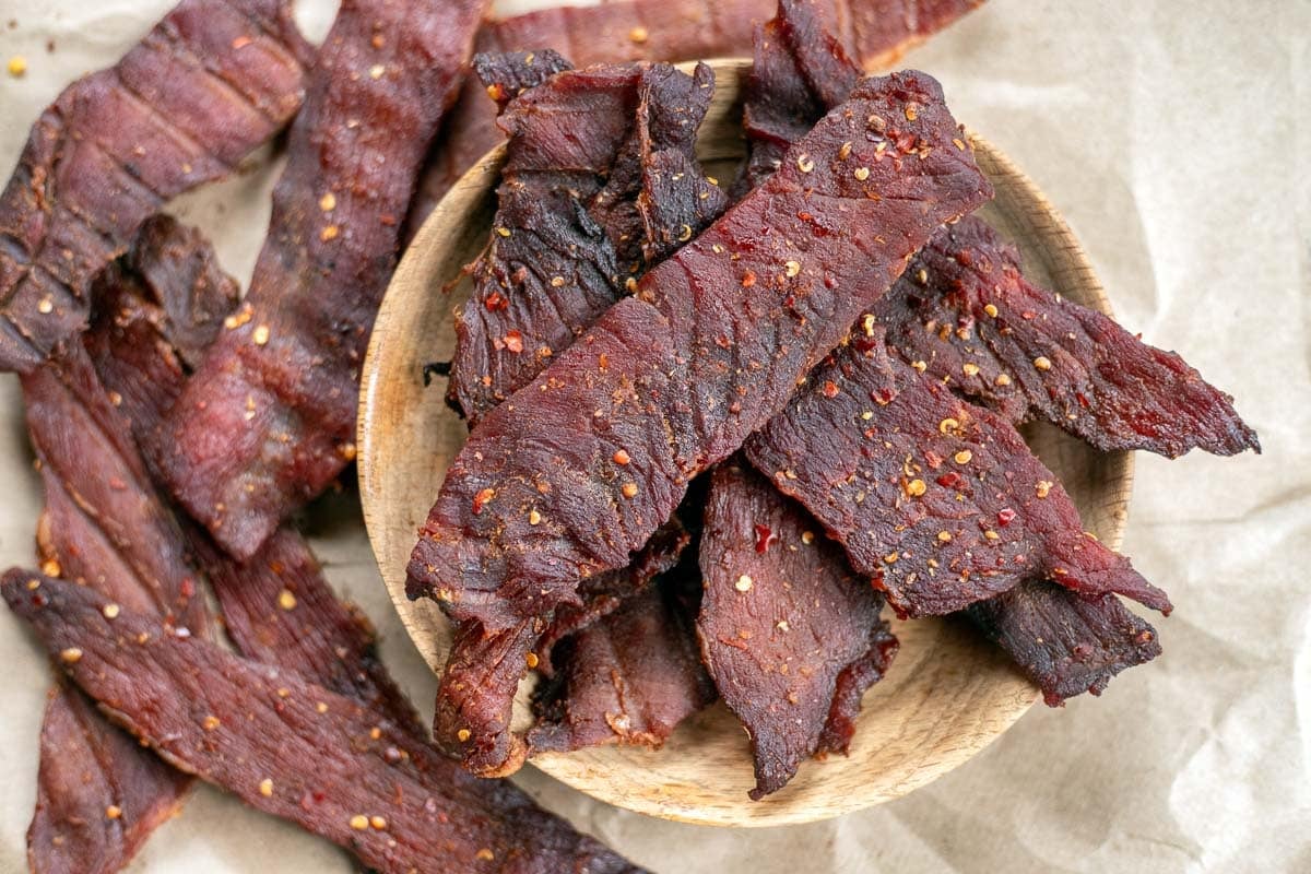 smoked beef jerky in a wooden bowl with more jerky around it.