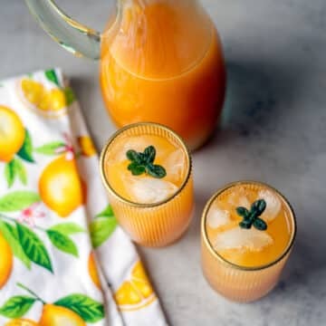 apricot nectar in 2 glasses with more in a pitcher and a folded dish towel.