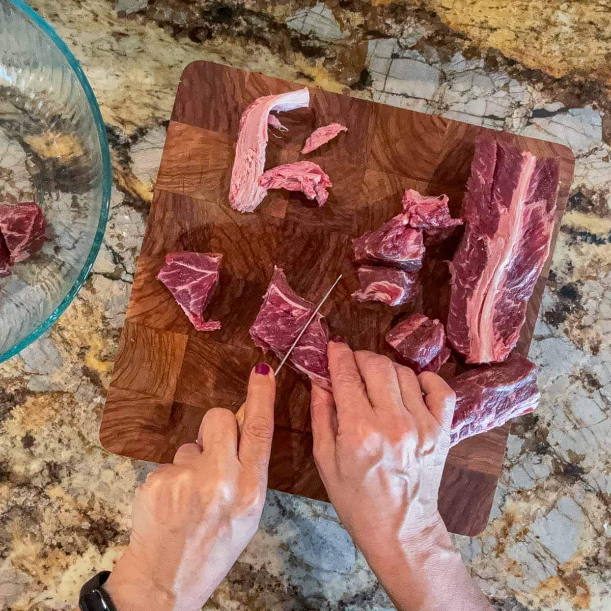 chopping beef into chunks on a cutting board. 