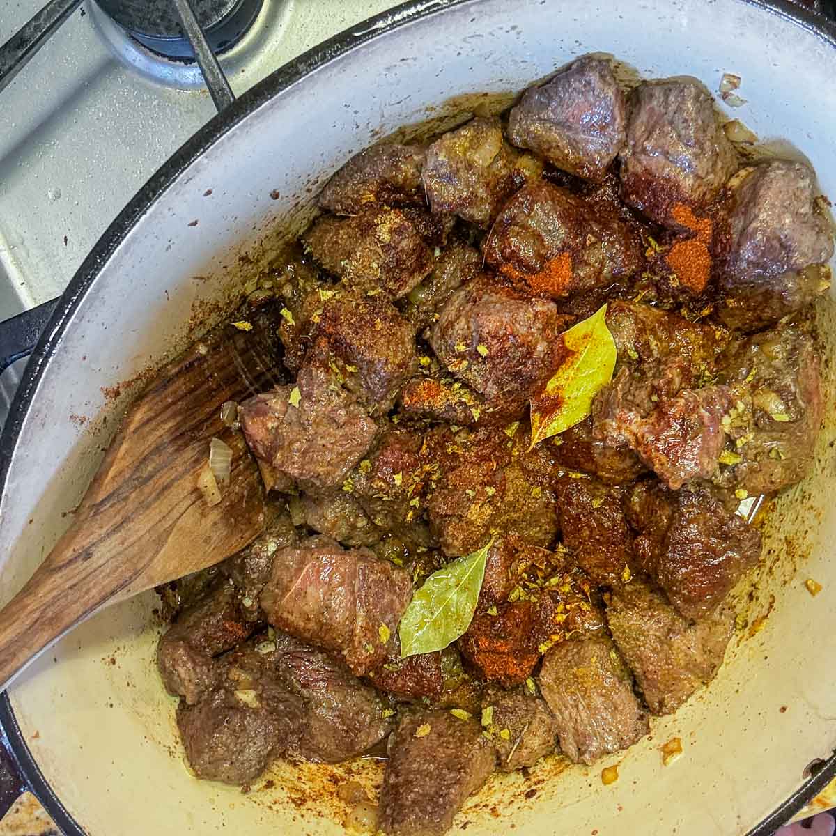 cooked cubed meat in a pot with spices and a wooden spoon.