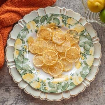 dried lemon slices on a plate with an orange towel and lemons and limes in a bowl next to them.