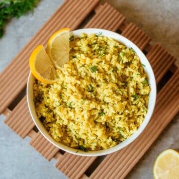 lemon dill rice in bowl with sliced lemons and fresh dill off to the side.