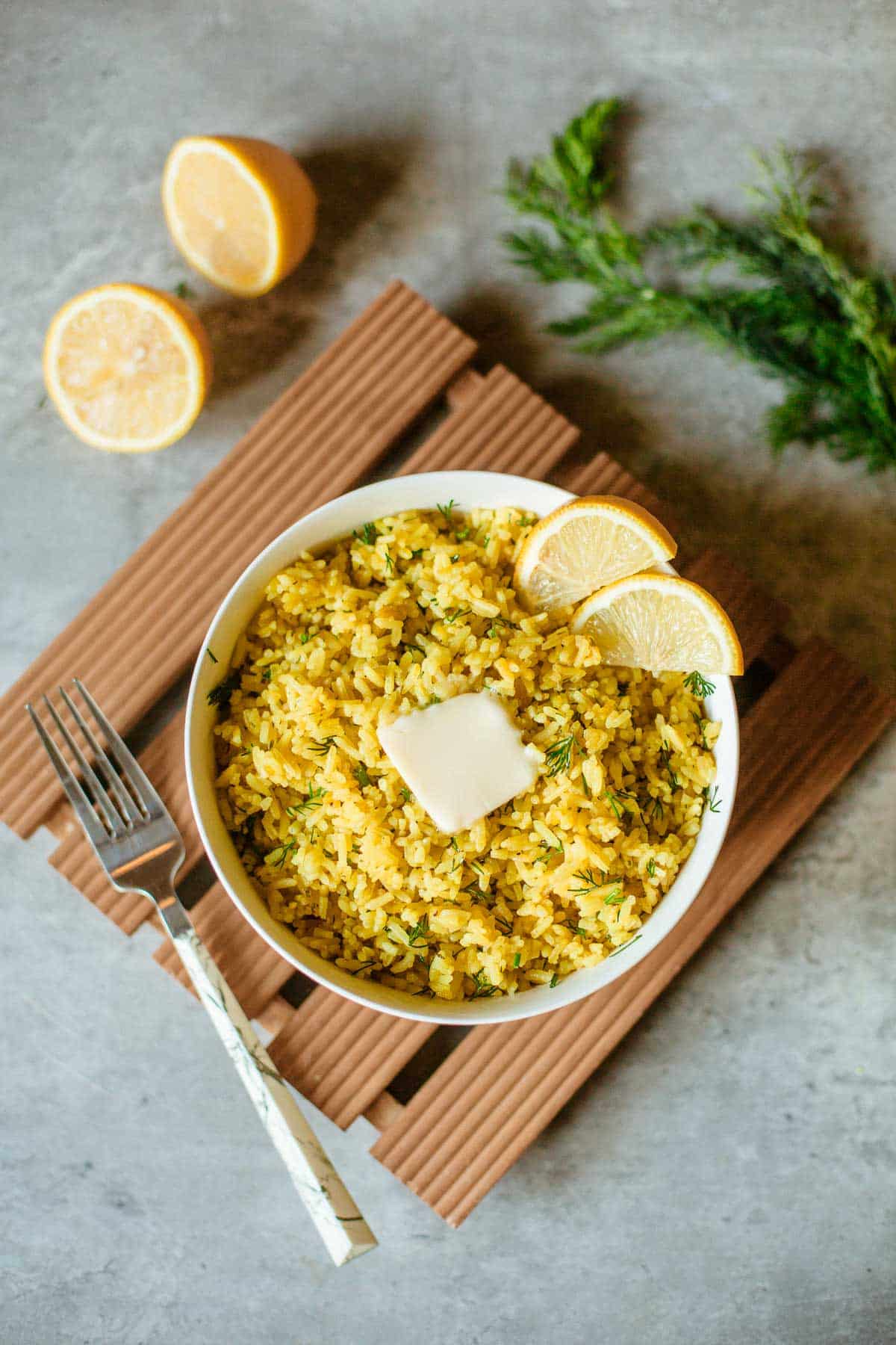 lemon dill rice in bowl with fork, sliced lemons and fresh dill off to the side.